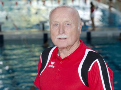 Trainer Alfred Liebrenz im roten T-Shirt. Im Hintergrund ein Schwimmbecken.